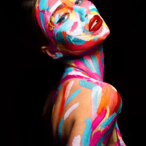 A model with a vibrant, multicolored paint covering her face and body against a black background.