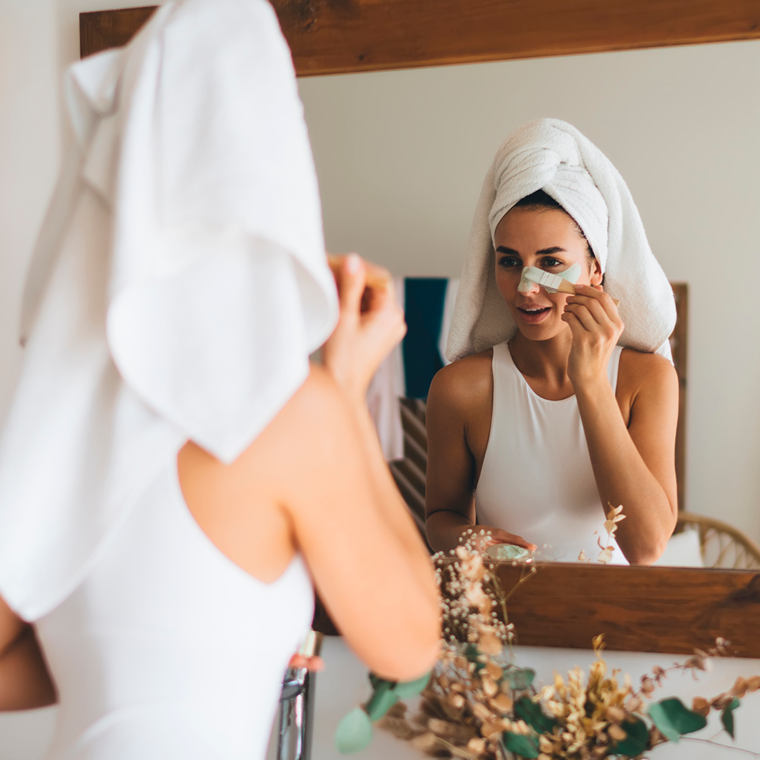 A woman applying under-eye patches while looking in the mirror. PRP Therapy Solutions