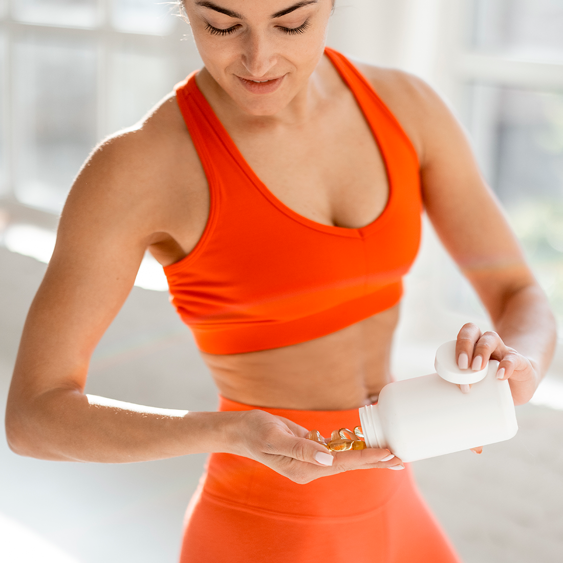 A fit woman in an orange sports bra and leggings pouring supplements from a bottle into her hand. PRP Therapy Solutions